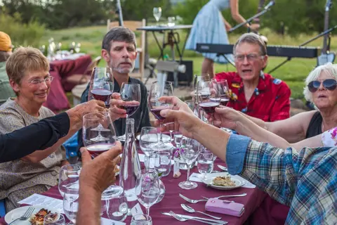 A group of people enjoying an outdoor wine tasting dinner, toasting with wine glasses.