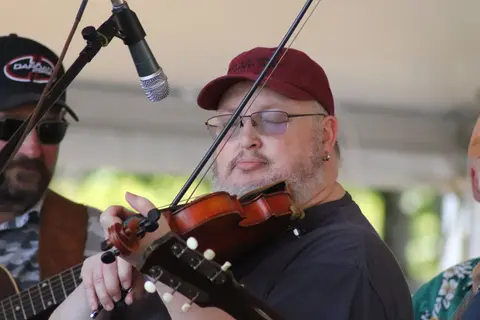 A man playing a fiddle while other musicians stand nearby.