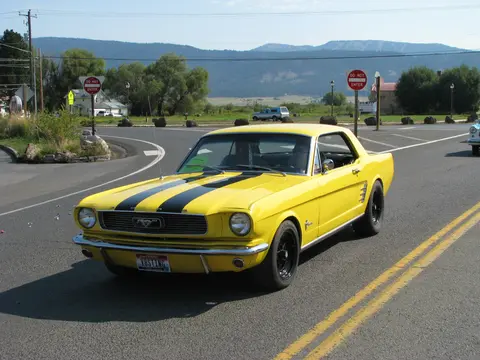 A yellow car with black racing stripes drives on an asphalt road.