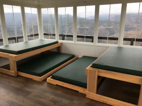 An interior view of a room with wooden bunk beds and large windows showing a mountain landscape.