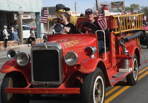 People ride in a vintage fire truck during a parade.