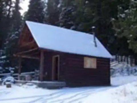A log cabin in the snow surrounded by trees.