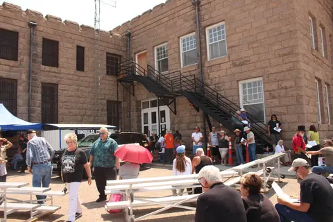 People gather outside a historic stone building with an exterior metal staircase.