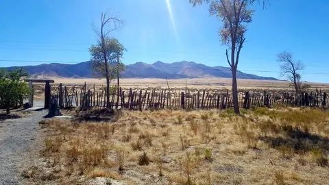 A rustic wooden fence borders a dry field with mountains in the background under a bright sky.