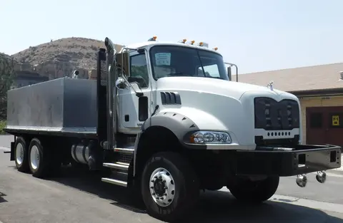 A white utility truck is parked outside with a large metal tank on the flatbed.