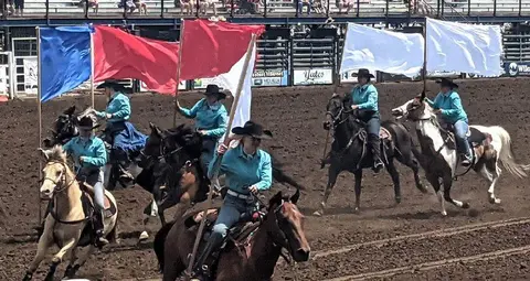 Several horse riders carrying flags in an arena.