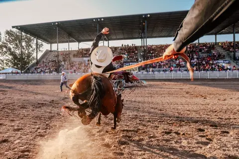 A cowboy rides a bucking horse at a rodeo arena.