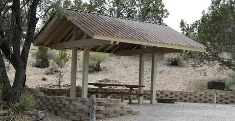 A covered picnic shelter with wooden tables stands outdoors in a desert landscape.