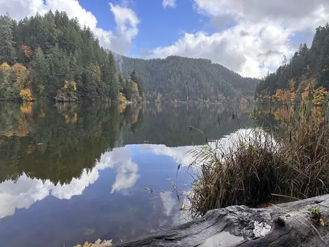 A scenic lake reflecting forested mountains and clouds in the sky.