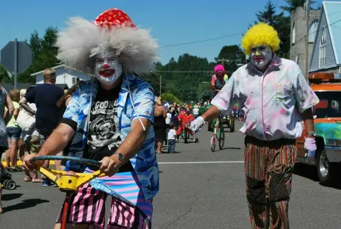 Two people dressed as clowns participate in a parade on a street.