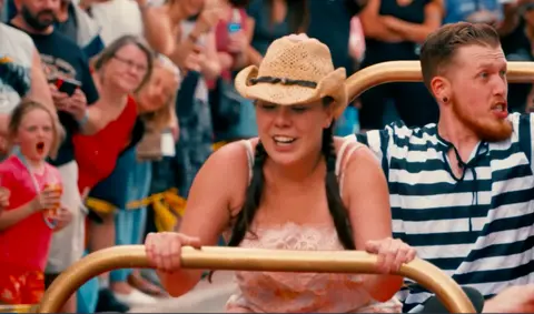 People riding a ride with a crowd watching in the background.