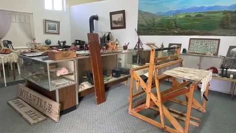 An interior view of a museum with historical artifacts, display cases, and a wooden loom.