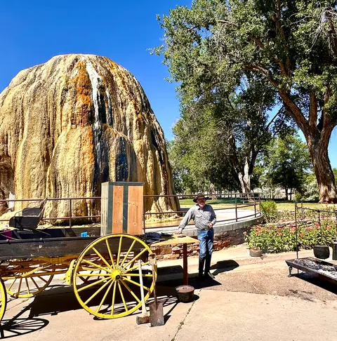 A man stands next to a wooden cart in front of a large travertine formation.