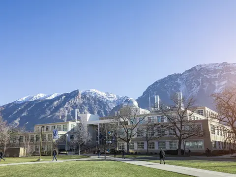 A large building with a dome on top stands in front of snow-capped mountains.