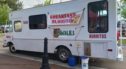 A white food truck parked on a street with banners advertising food items.