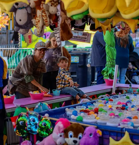 People play a carnival game surrounded by stuffed animals.