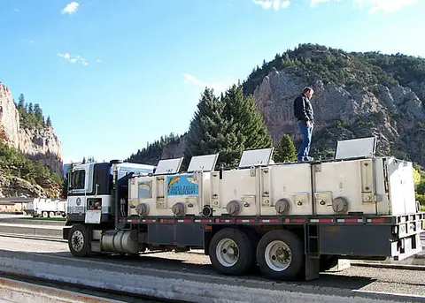 A person stands on top of a large fish hauling truck outdoors in a mountainous landscape.