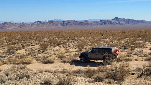 An off-road vehicle parked in a vast desert landscape with distant mountains.