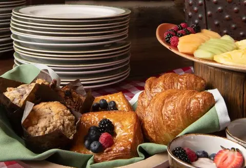 A breakfast buffet with pastries, fruit, and stacks of plates.