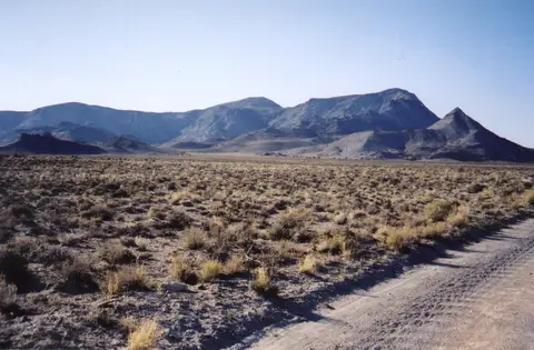 A dirt road winds through a sparse desert landscape toward distant mountains.