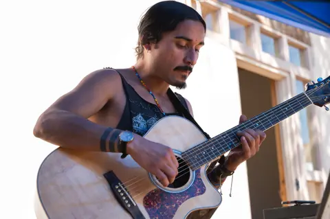 A man plays an acoustic guitar outdoors.