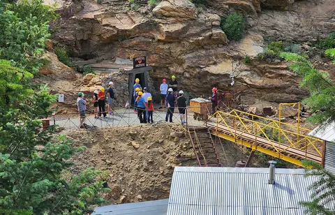 A group of visitors wearing hard hats stands outside a mine entrance.