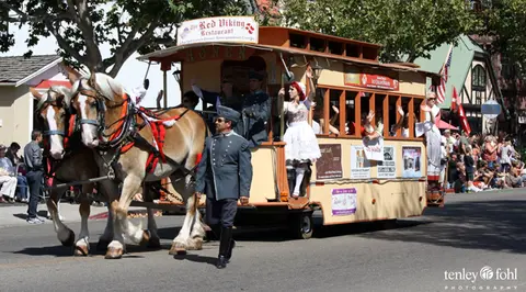 A horse-drawn trolley with people in costume participates in a street parade.
