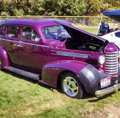 A purple vintage car parked on grass with its hood open.