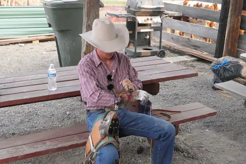 A cowboy sits on a picnic table adjusting his gear.