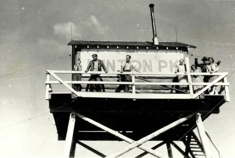 A historic black and white photograph showing people standing on a wooden lookout tower.