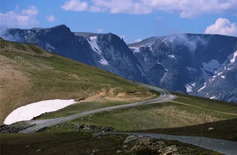 A winding road through a mountainous landscape with patches of snow.